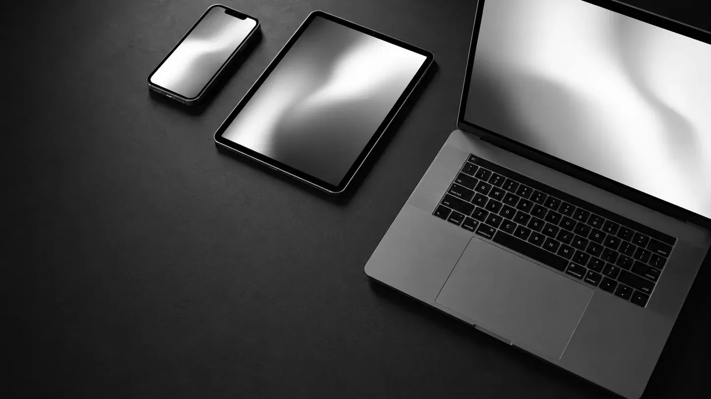 Un teléfono, una tableta y un portátil alineados y separados sobre un escritorio oscuro