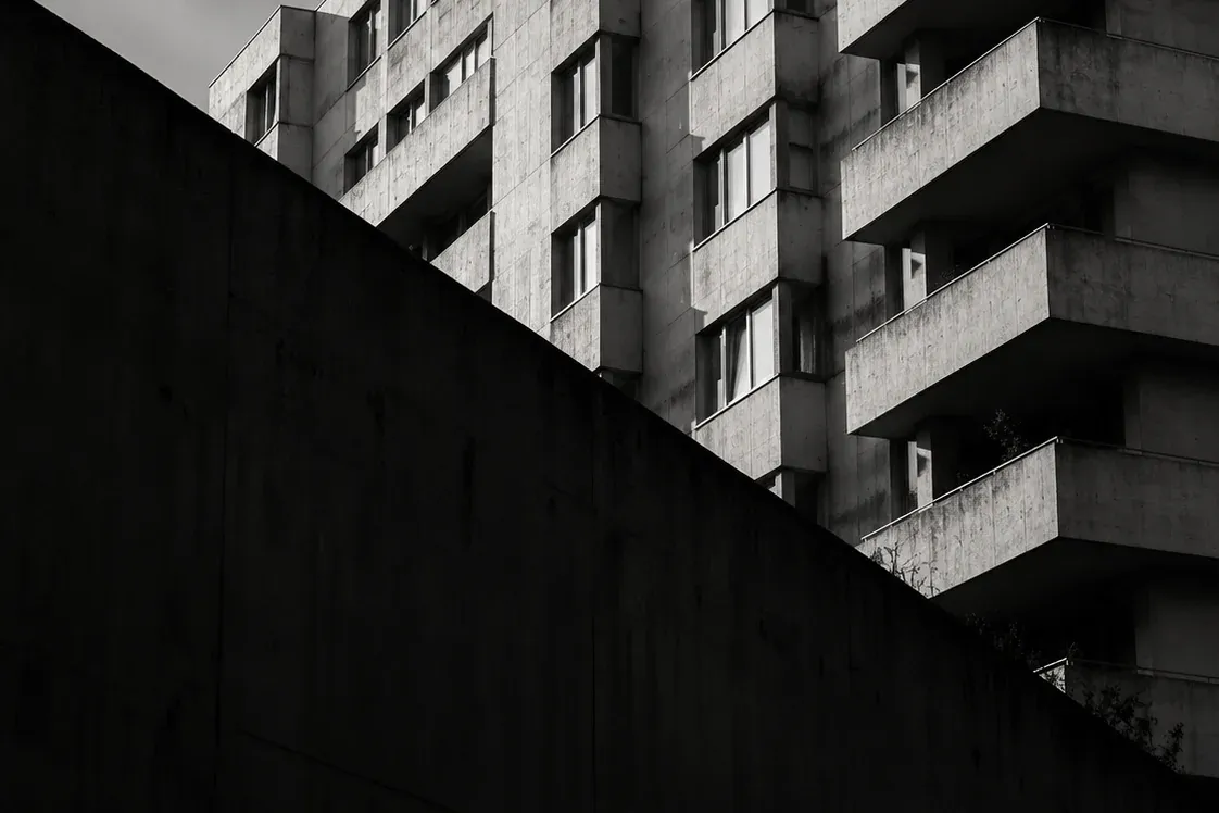 Muro de hormigón en sombra en primer plano y la fachada de un edificio residencial detrás