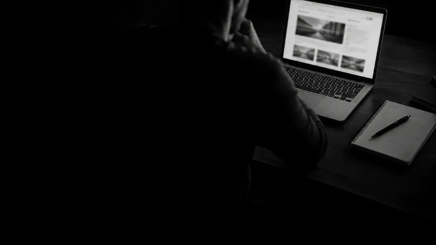 Persona de espaldas frente a un portátil que muestra un sitio web, con una libreta al lado